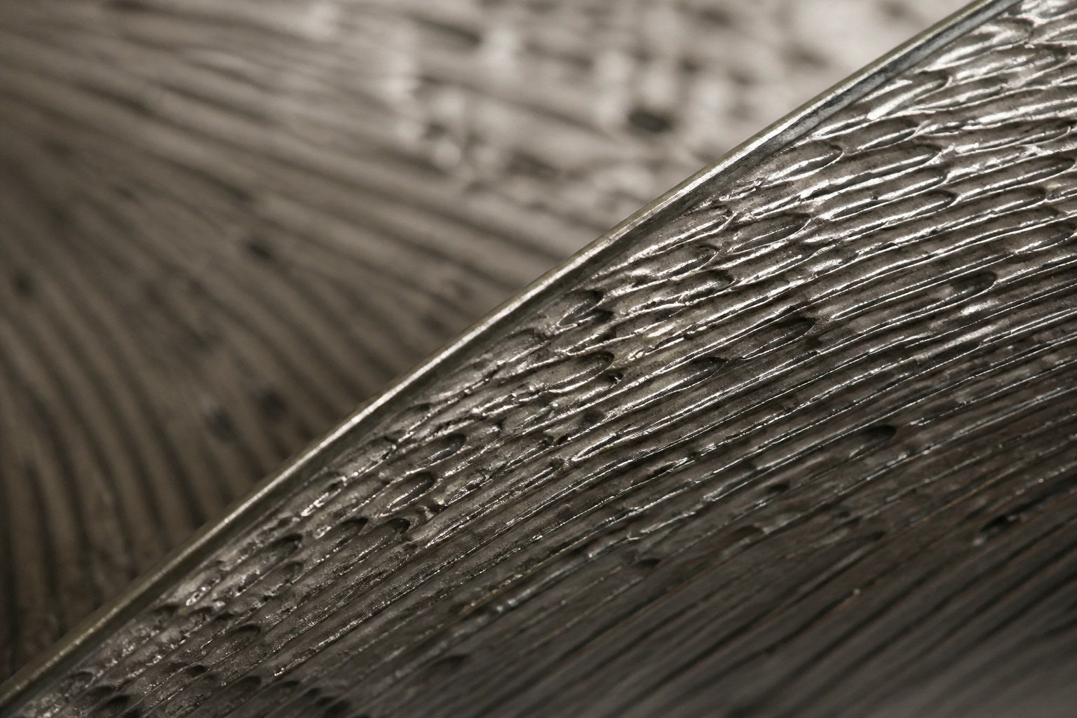 Wide woven-wire infinity form in pale silver-grey with two lens voids, against a plaster wall.