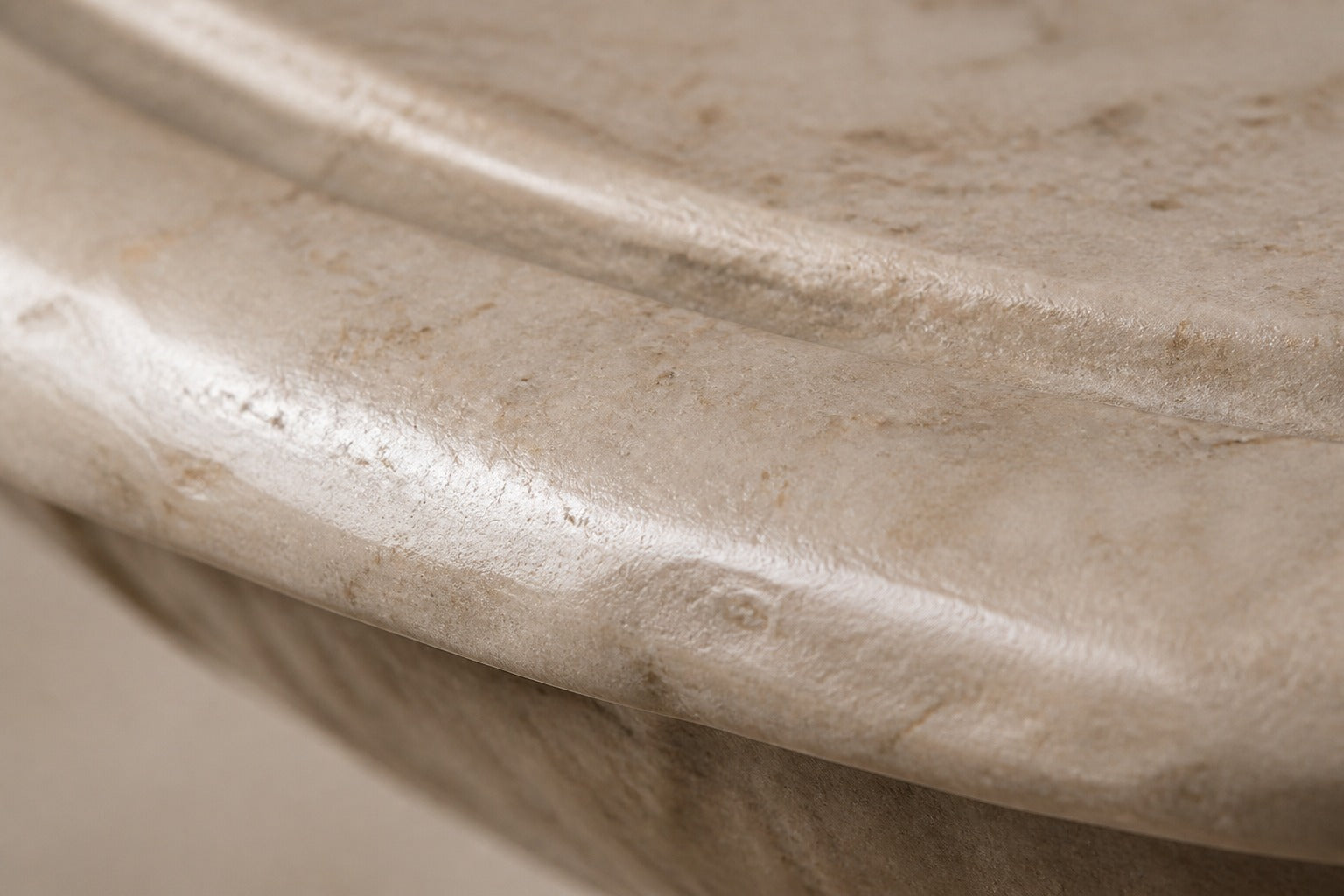 Pale limestone pedestal fountain Fontena Ø65, cream with open fossil speckle, on a pale stone floor.