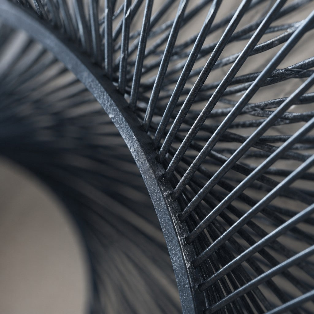 Deep indigo steel wall sculpture Chiocciola, fine wire wound across a circular rim into a spiral void, on a plaster wall.