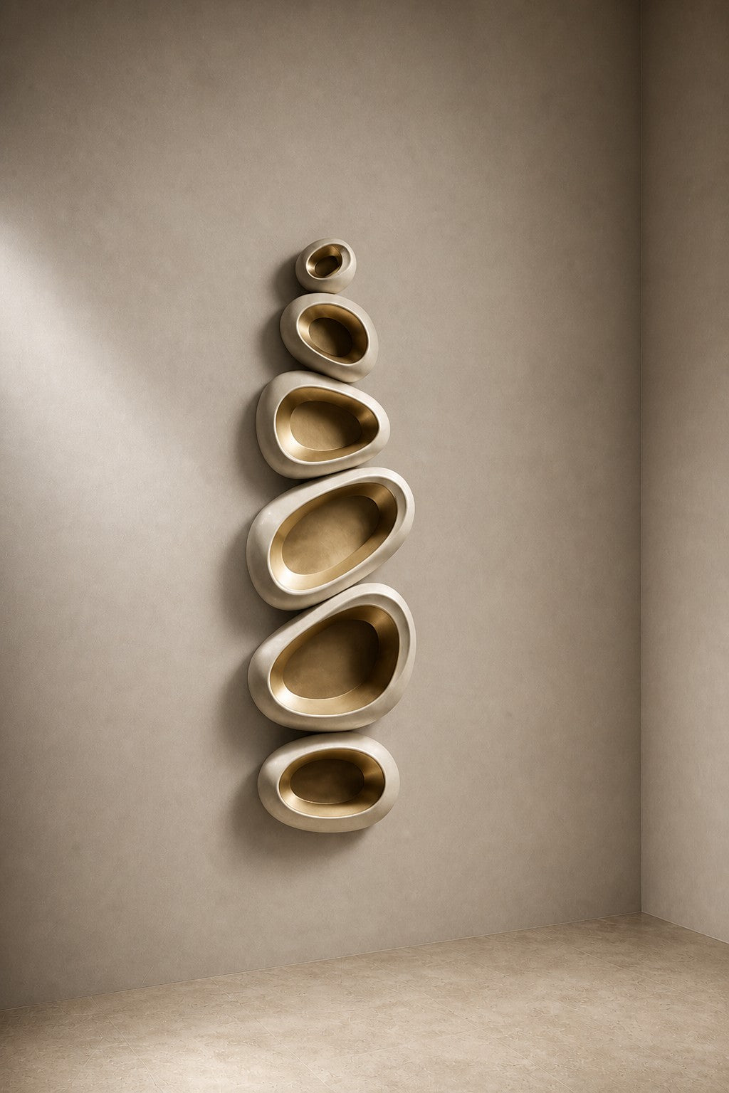 Champagne gold bronze wall sculpture Guijarro, a continuous folded ribbon swelling to a smooth belly, on a plaster wall.
