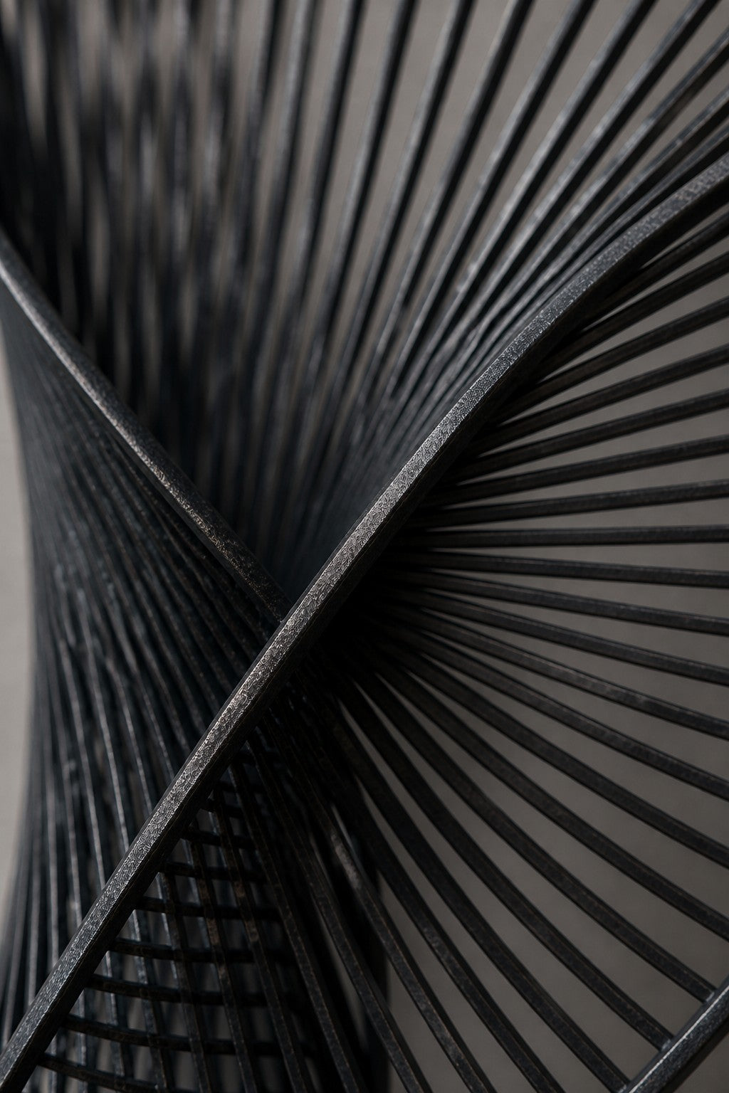 Graphite steel wall sculpture Iltifat, a single sheet folded through itself in one continuous turn, on a plaster wall.