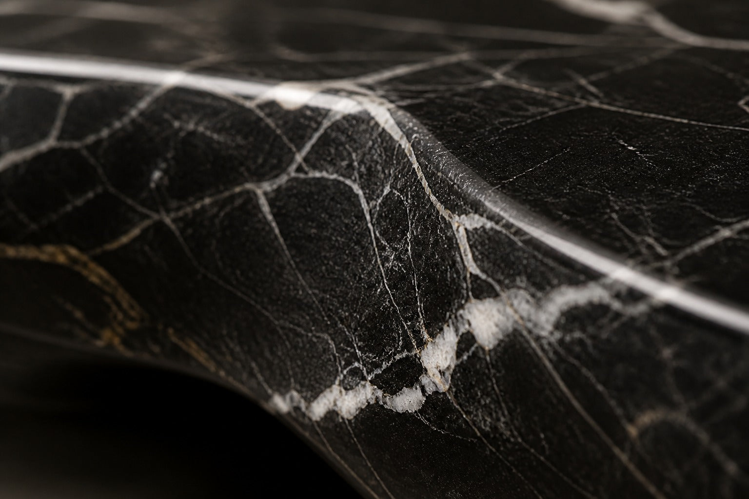Black marble with white veining fire table Laylan 220, deep black with white and gold veining, on a pale stone floor.