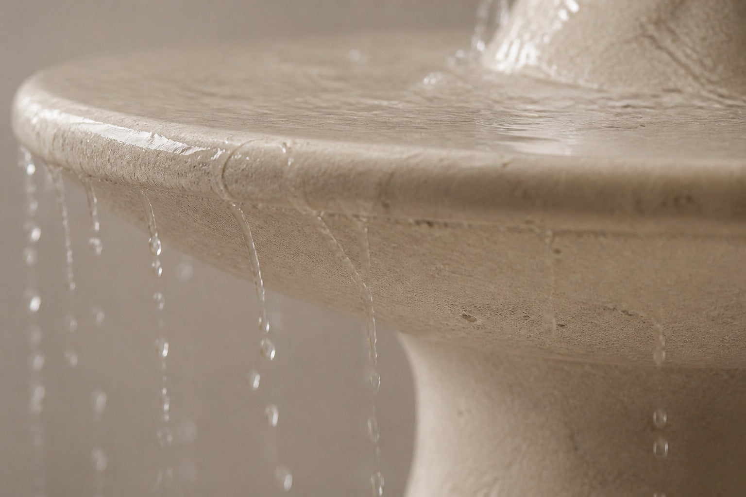 Pale limestone pedestal fountain Marena Ø65, dark bronze with a pale verdigris stem, on a pale stone floor.