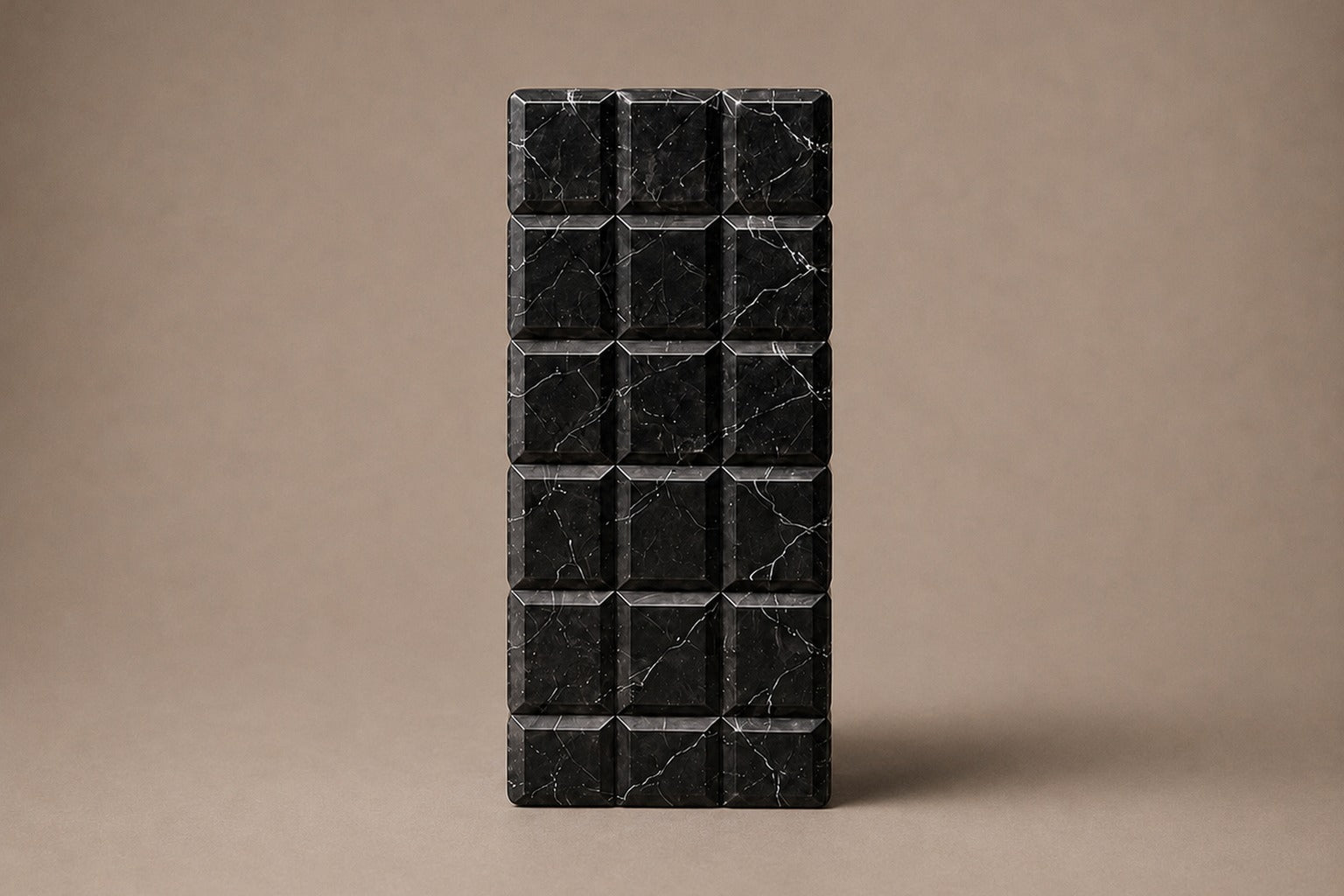 Tall black Nero Marquina marble column carved into a grid of raised cushioned panels.