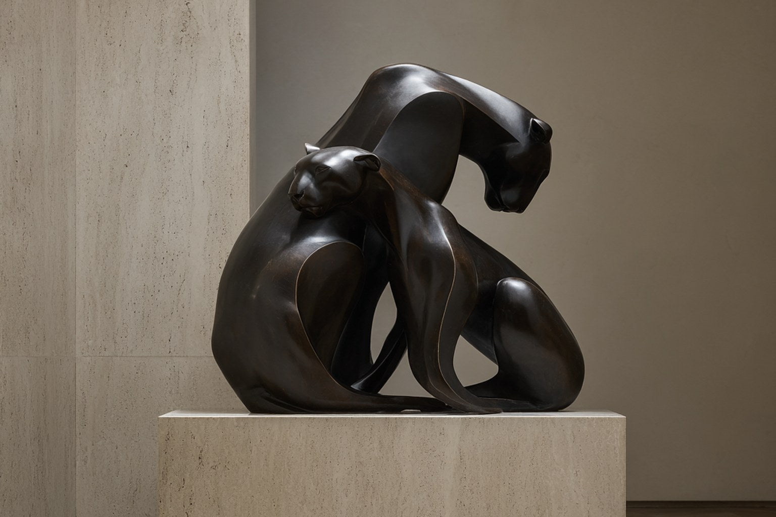 Near-black patinated bronze sculpture Pedregal, two big-cat figures entwined as a single mass, shown on a travertine display plinth.