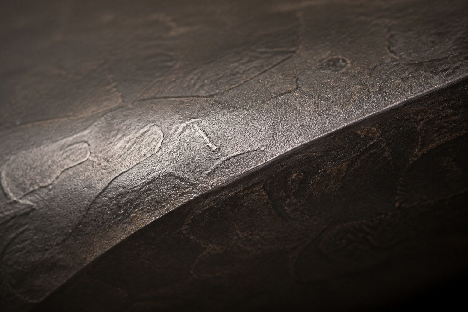 Charcoal-bronze stone fire table Suiran 220, charcoal with a warm bronze cast, on a pale stone floor.
