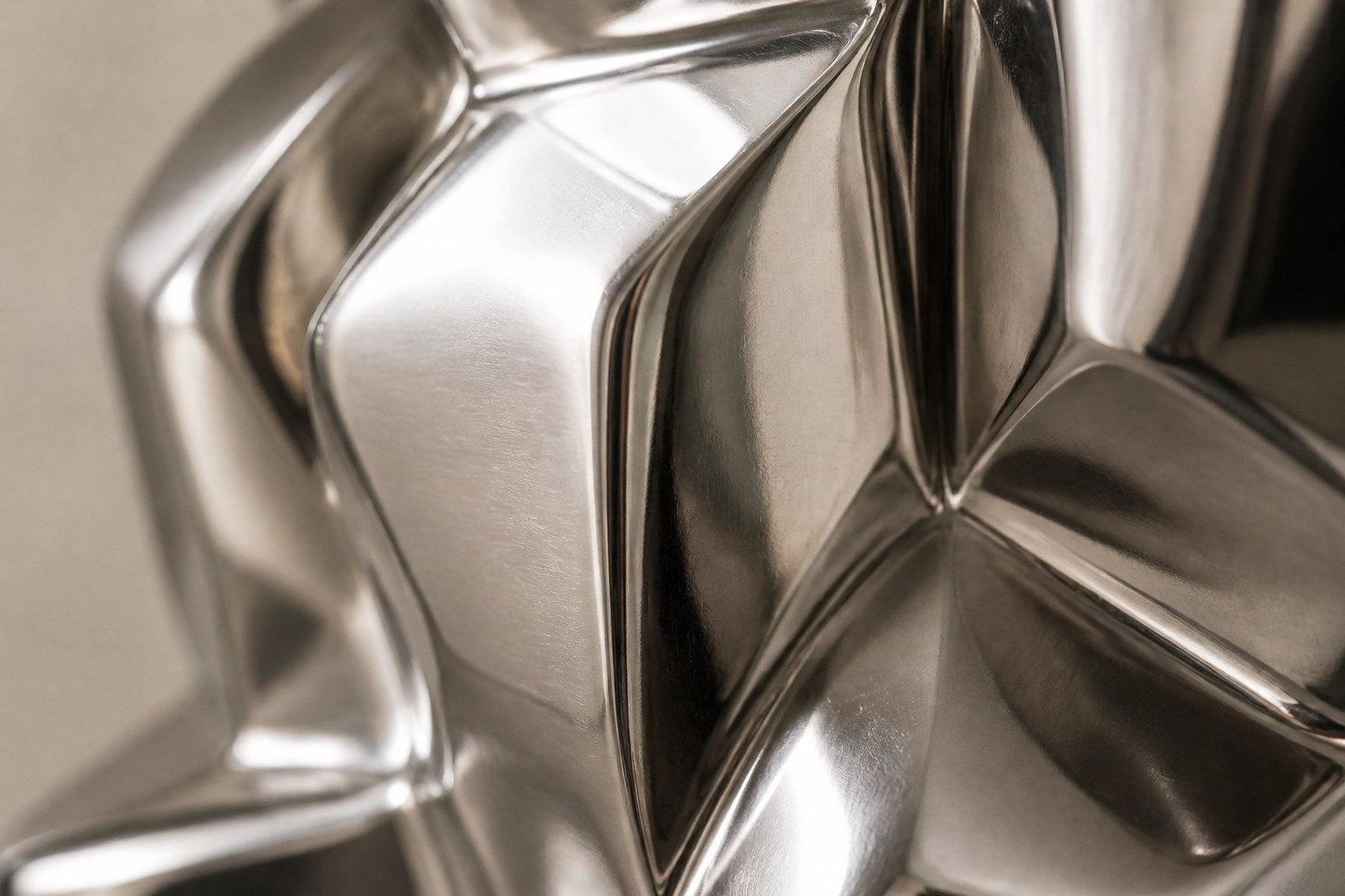 Mirror-polished stainless steel sculpture Alkaid, a column of stacked interlocking blocks, on a white marble cube plinth.