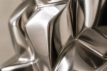 Mirror-polished stainless steel sculpture Alkaid, a column of stacked interlocking blocks, on a white marble cube plinth.