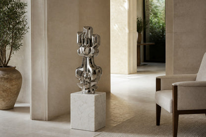 Mirror-polished stainless steel sculpture Alkaid, a column of stacked interlocking blocks, on a white marble cube plinth.