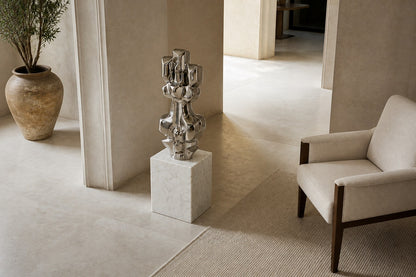 Mirror-polished stainless steel sculpture Alkaid, a column of stacked interlocking blocks, on a white marble cube plinth.