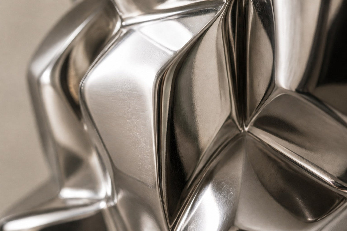 Mirror-polished stainless steel sculpture Alkaid, a column of stacked interlocking blocks, on a white marble cube plinth.