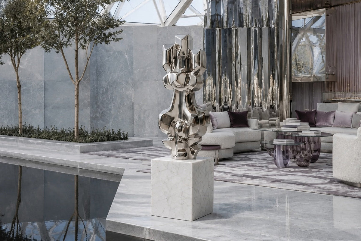 Mirror-polished stainless steel sculpture Alkaid, a column of stacked interlocking blocks, on a white marble cube plinth.