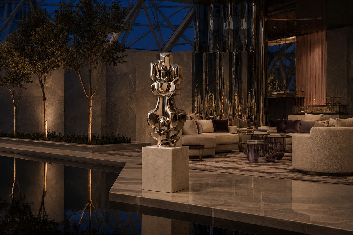 Mirror-polished stainless steel sculpture Alkaid, a column of stacked interlocking blocks, on a white marble cube plinth.