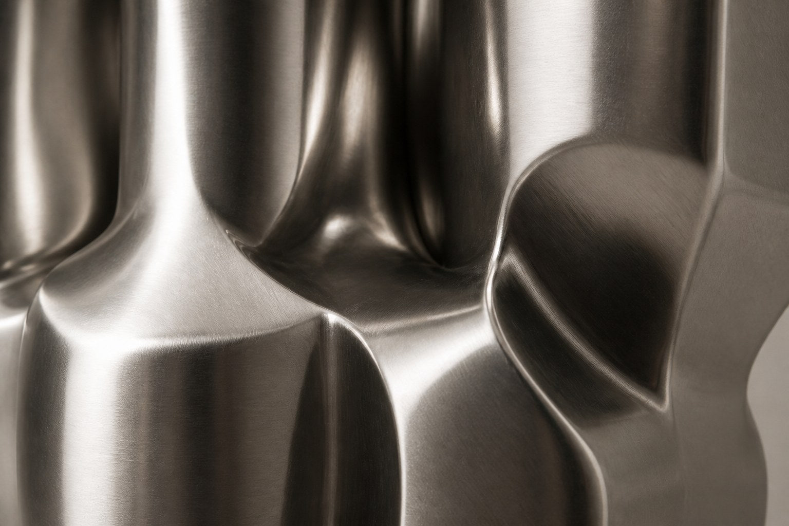 Brushed stainless steel sculpture Alphard, a column of stacked interlocking blocks, on a fluted brushed steel drum plinth.