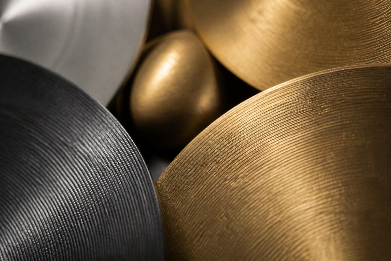 Cluster of overlapping spun discs in black, brass and pewter finishes on a plaster wall.
