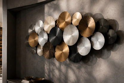 Cluster of overlapping spun discs in black, brass and pewter finishes on a plaster wall.