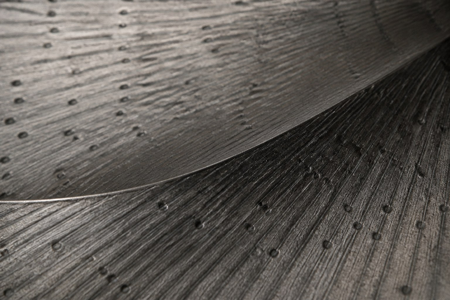 Broad woven-wire ellipse in pale grey with an open oval void, against a plaster wall.