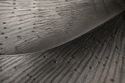 Broad woven-wire ellipse in pale grey with an open oval void, against a plaster wall.