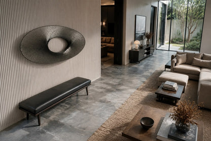 Broad woven-wire ellipse in pale grey with an open oval void, against a plaster wall.