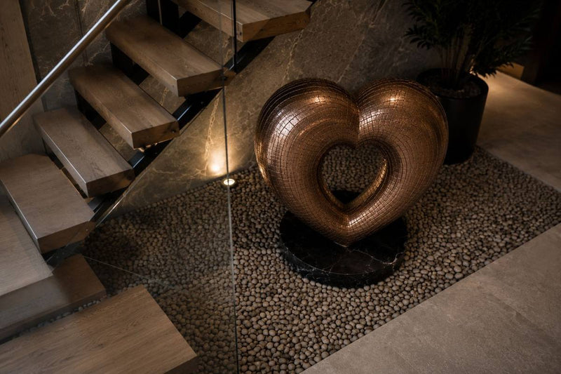 Woven bronze heart sculpture beside a timber staircase
