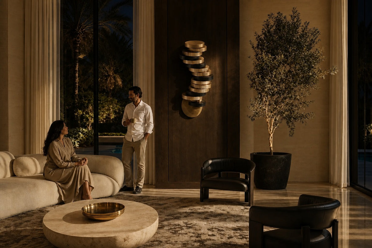 Cairn — 240 cm wall-mounted column of stacked ribbed brass and bronze discs, the same room at night, lamps on