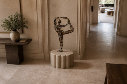Bronze strut-cage figure sculpture Centina in a backbend on one leg, gilt and blackened, on a fluted travertine drum plinth.