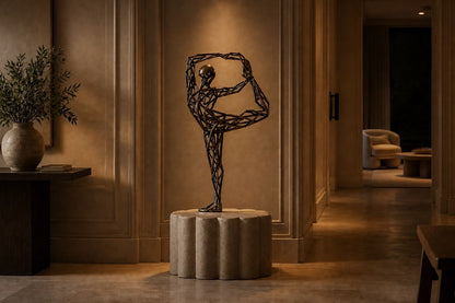 Bronze strut-cage figure sculpture Centina in a backbend on one leg, gilt and blackened, on a fluted travertine drum plinth.