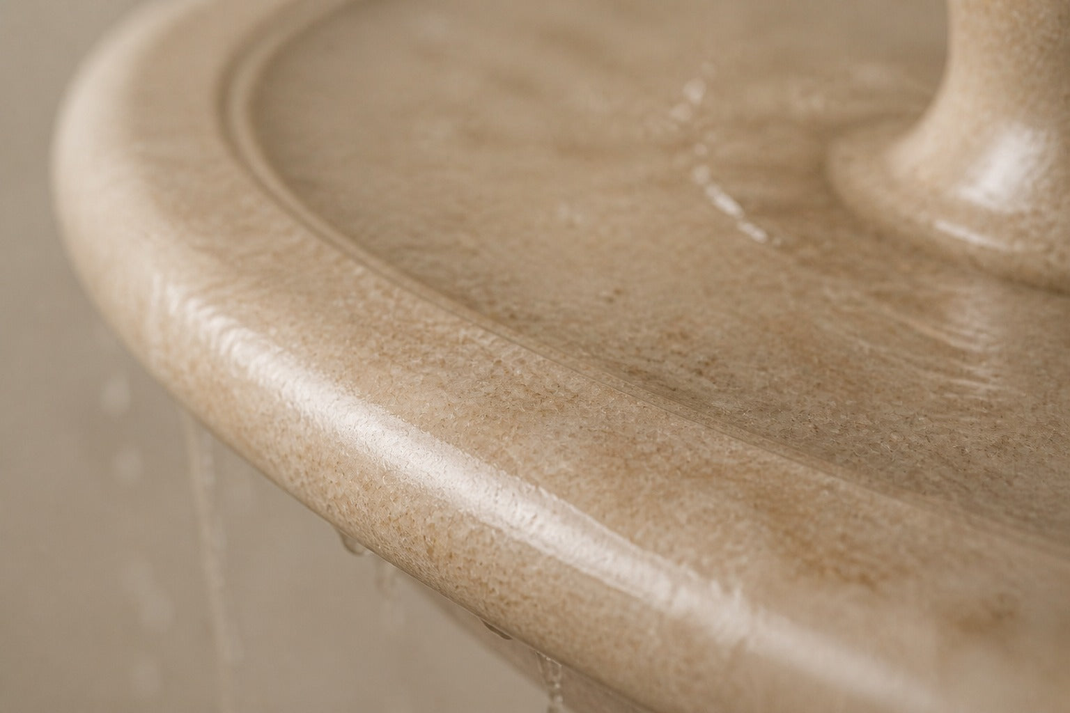 Pale limestone pedestal fountain Chiara Ø65, warm cream with fine fossil speckle, on a pale stone floor.