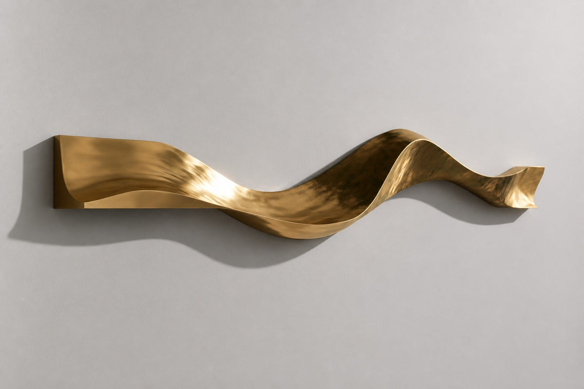 Cinta — polished brass ribbon wall sculpture in three soft waves, studio side angle showing its depth