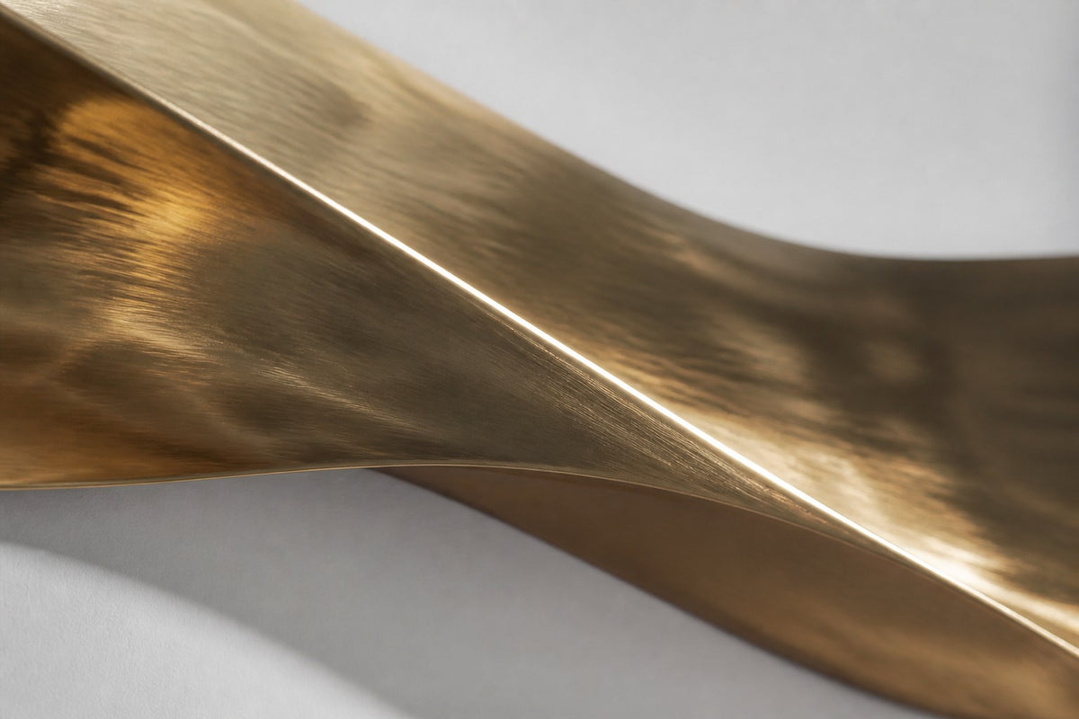 Cinta — polished brass ribbon wall sculpture in three soft waves, close detail of the surface and edge