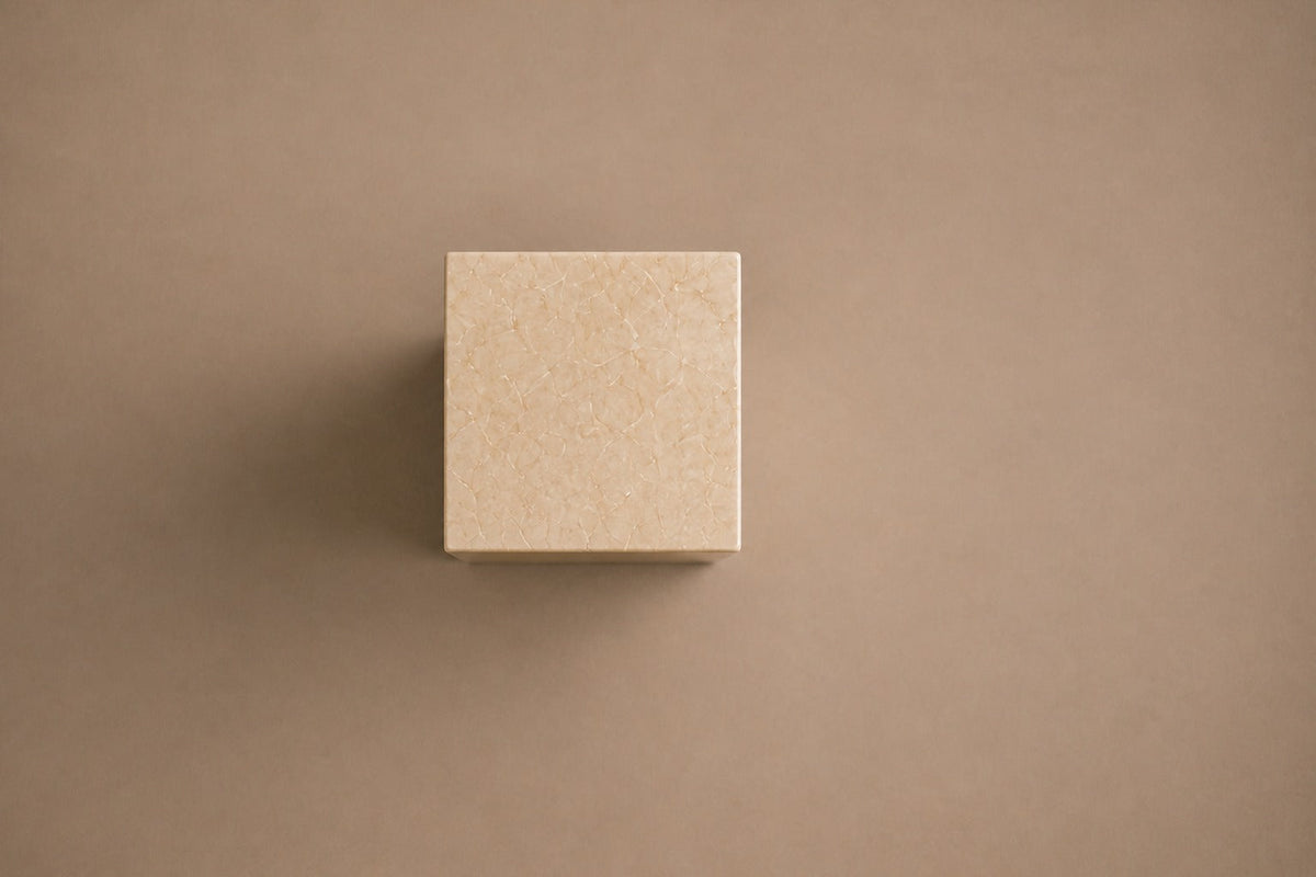 Tall cream Crema Marfil marble pedestal with a closed eye carved in shallow relief on one face — viewed from directly above
