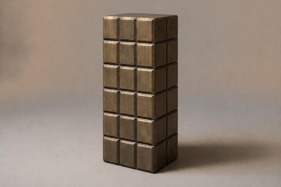 Tall antique bronze column built as a grid of raised cushioned panels — three-quarter studio view of the whole pedestal