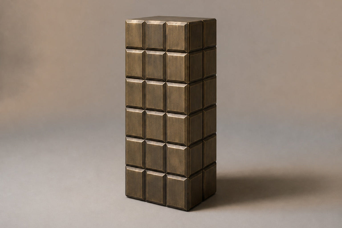 Tall antique bronze column built as a grid of raised cushioned panels — three-quarter studio view of the whole pedestal