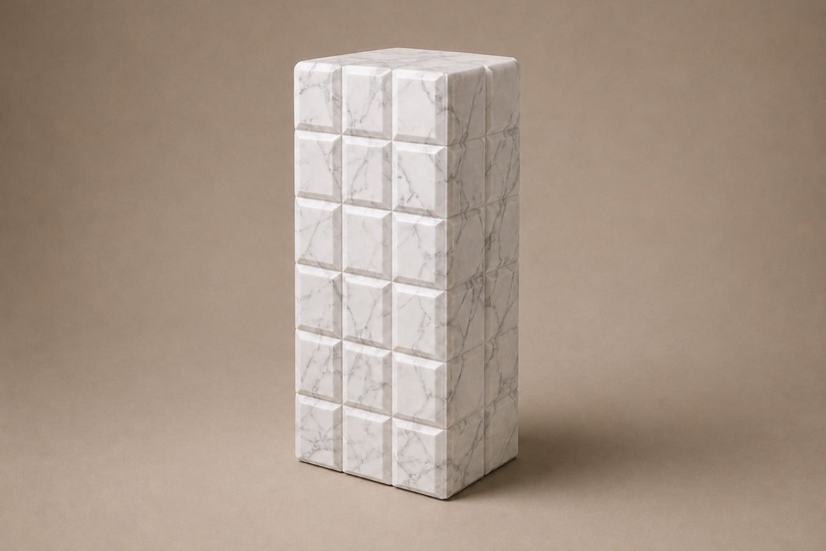 Tall white Carrara marble column carved into a grid of raised cushioned panels — three-quarter studio view of the whole pedestal