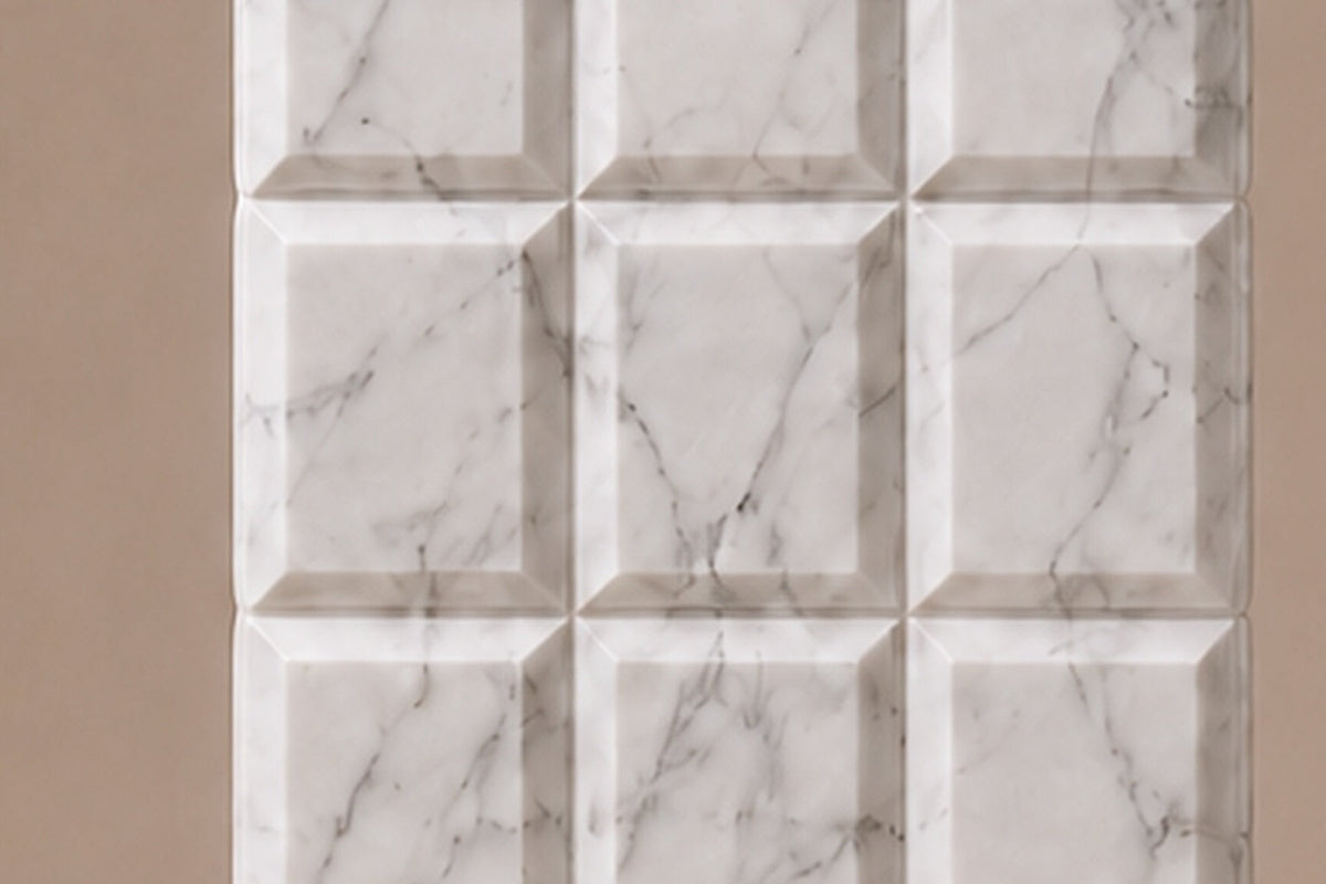 Tall white Carrara marble column carved into a grid of raised cushioned panels — close detail of the surface