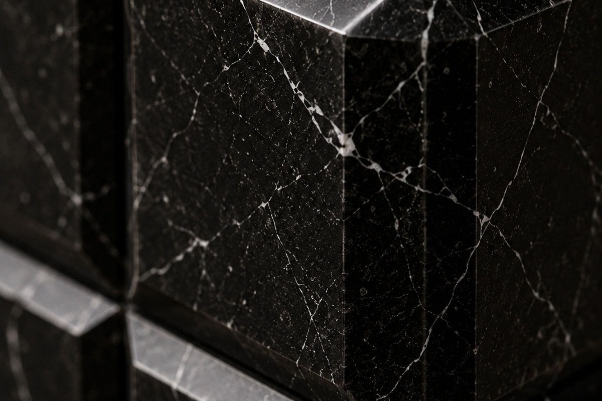 Tall black Nero Marquina marble column carved into a grid of raised cushioned panels — close detail of the surface