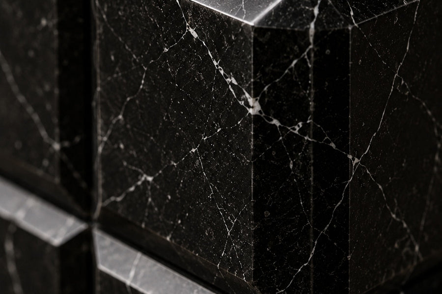 Tall black Nero Marquina marble column carved into a grid of raised cushioned panels — close detail of the surface