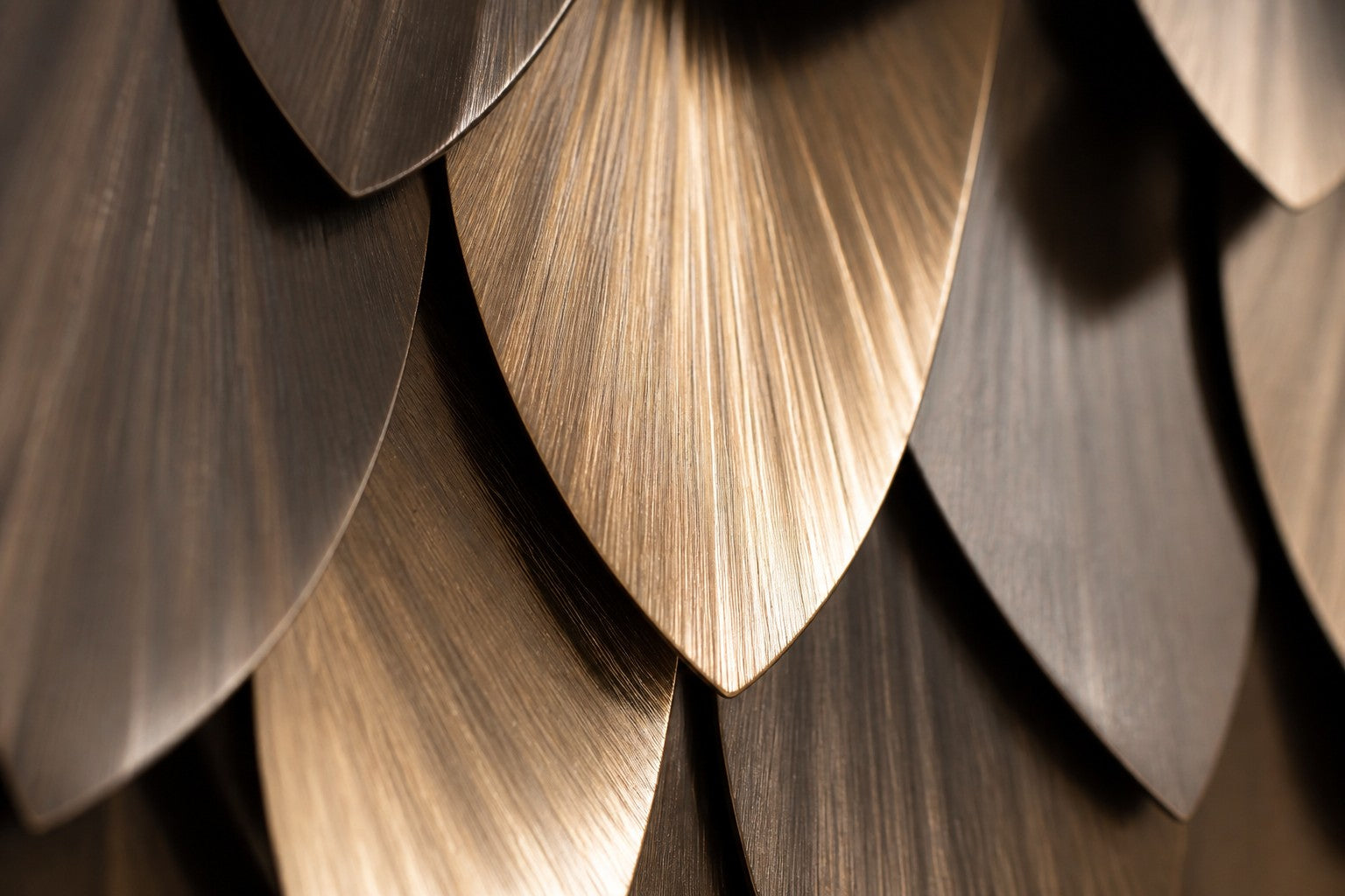 Warm antique gold brass wall sculpture Dhahab, overlapping leaf plates shingled on a concealed rail, on a plaster wall.