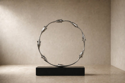 Mirror-polished stainless steel ring sculpture Estero Ø70, eight linked forms nose to tail, on a black granite block.