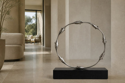 Mirror-polished stainless steel ring sculpture Estero Ø70, eight linked forms nose to tail, on a black granite block.