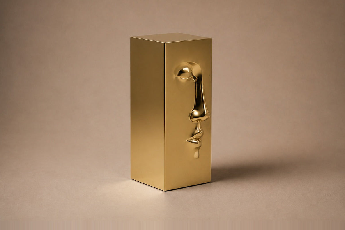 Tall gold PVD pedestal with a closed eye, nose and mouth formed seamlessly out of one face — three-quarter studio view of the whole pedestal