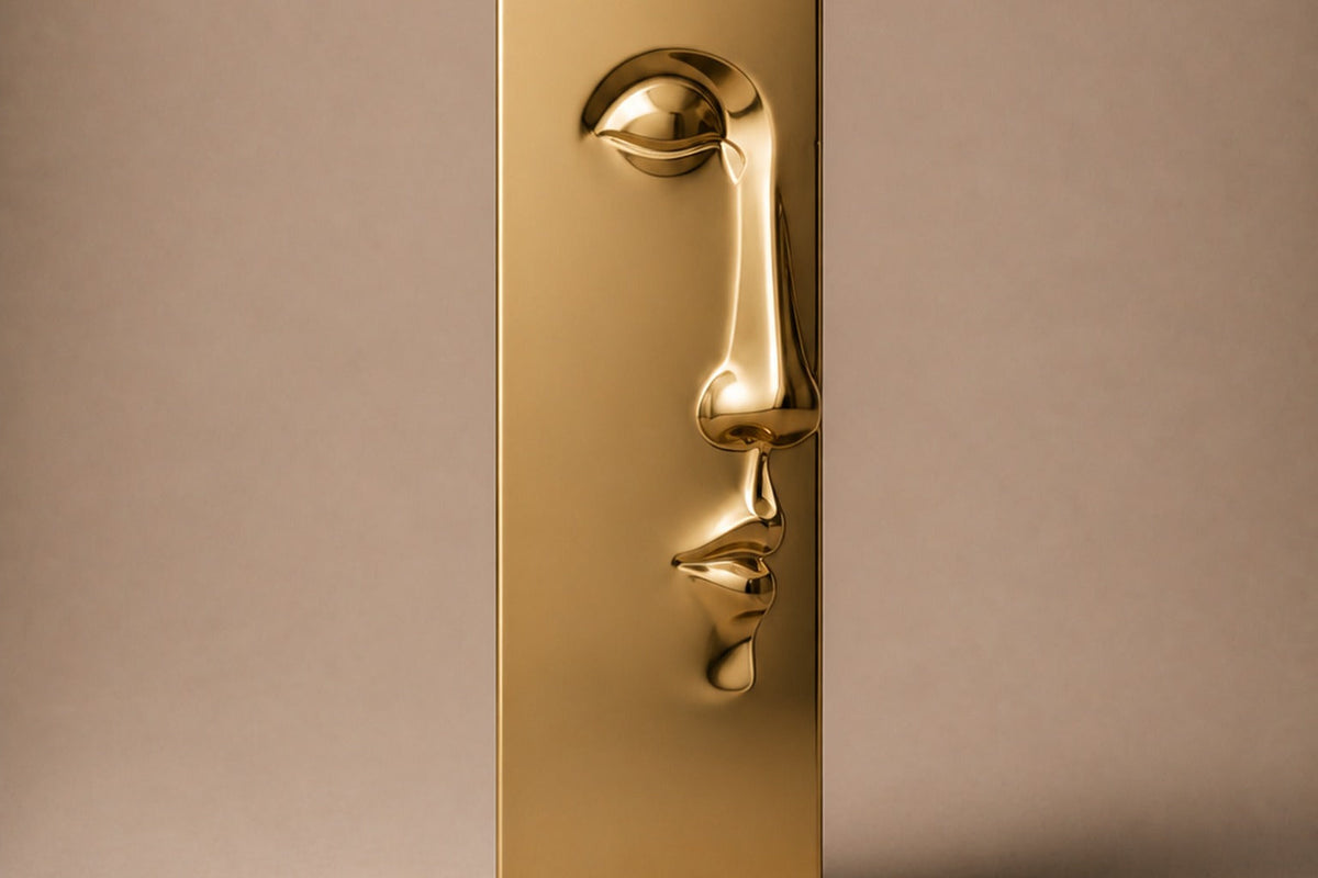 Tall gold PVD pedestal with a closed eye, nose and mouth formed seamlessly out of one face — front elevation