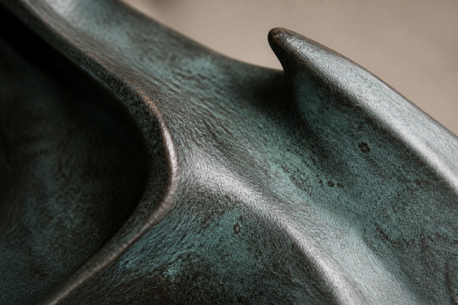 Blue-patinated bronze ring sculpture Farallon Ø60, four winged forms overlapping into a circle, on a black granite block.