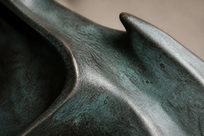 Blue-patinated bronze ring sculpture Farallon Ø60, four winged forms overlapping into a circle, on a black granite block.