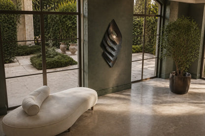Dark bronze bronze wall sculpture Gemma, a single faceted lozenge in shallow relief, on a plaster wall.