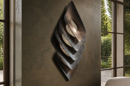 Dark bronze bronze wall sculpture Gemma, a single faceted lozenge in shallow relief, on a plaster wall.