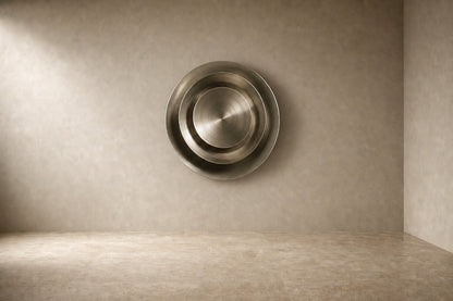 Bright silver stainless steel wall sculpture Plata, nested spun dishes stepping to a turned centre, on a plaster wall.