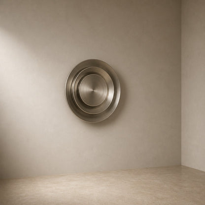Bright silver stainless steel wall sculpture Plata, nested spun dishes stepping to a turned centre, on a plaster wall.