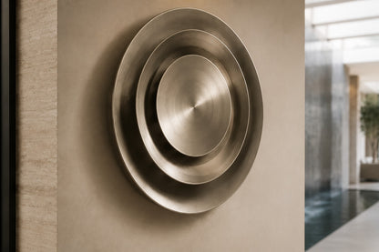 Bright silver stainless steel wall sculpture Plata, nested spun dishes stepping to a turned centre, on a plaster wall.