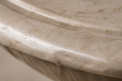 Pale limestone pedestal fountain Fontena Ø65, cream with open fossil speckle, on a pale stone floor.
